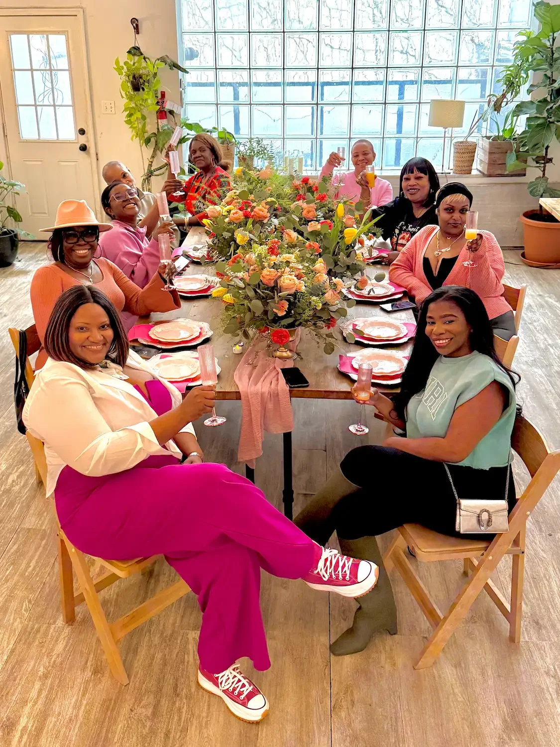 Friends toasting at a styled birthday party table with a floral centerpiece at Bat Haus in Williamsburg, Brooklyn.