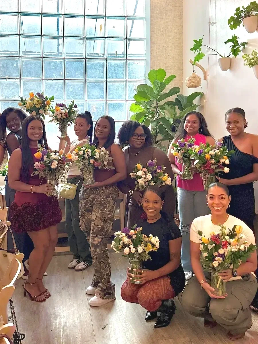 Friends celebrating a birthday with handmade bouquets by the glass-block window at Bat Haus in Brooklyn.