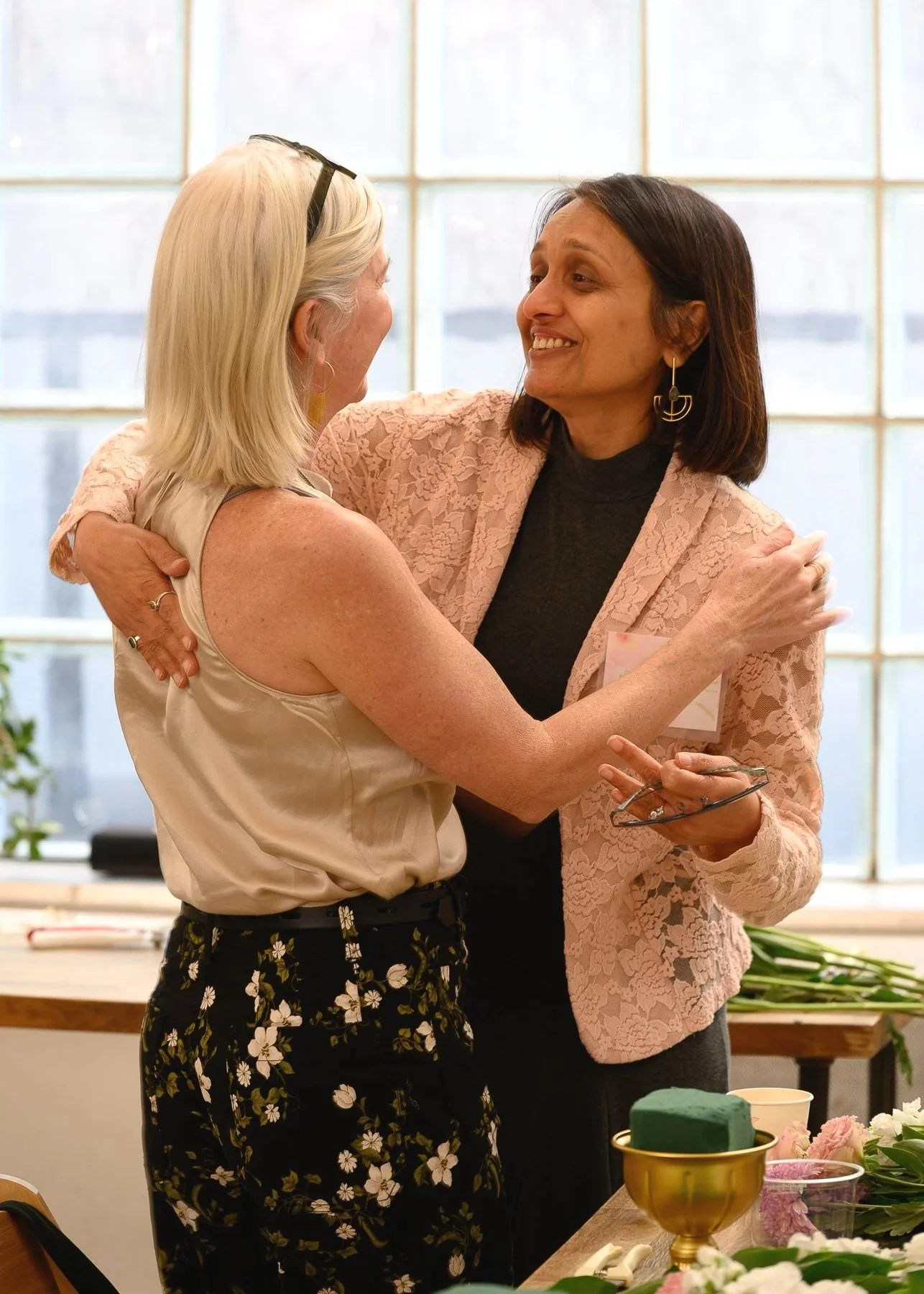 Two finance team members sharing a hug at a corporate floral workshop at Bat Haus in Williamsburg, Brooklyn.