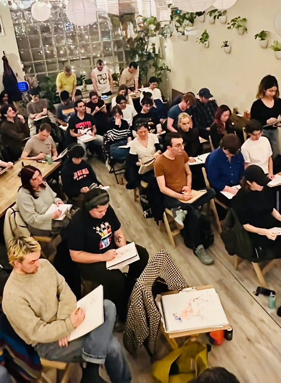 Full room of artists sketching during Drink n’ Draw at Bat Haus in Williamsburg Brooklyn, weekly Wednesday figure drawing night with easels and paper lantern lights.