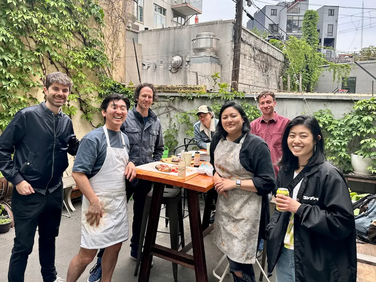 Group in aprons gathered around a high-top table during a workshop in the private backyard at Bat Haus event space in Brooklyn.