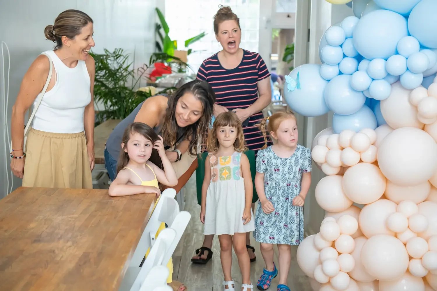 Children and parents gathered at a kids' birthday party with a blue-and-cream balloon garland at Bat Haus in Brooklyn.