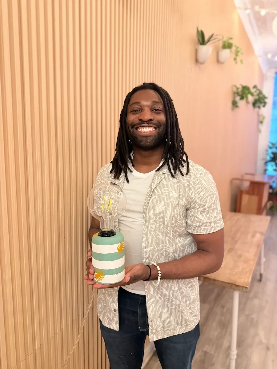A guest holding his handmade striped lamp at a lamp-making workshop at Bat Haus in Williamsburg, Brooklyn.