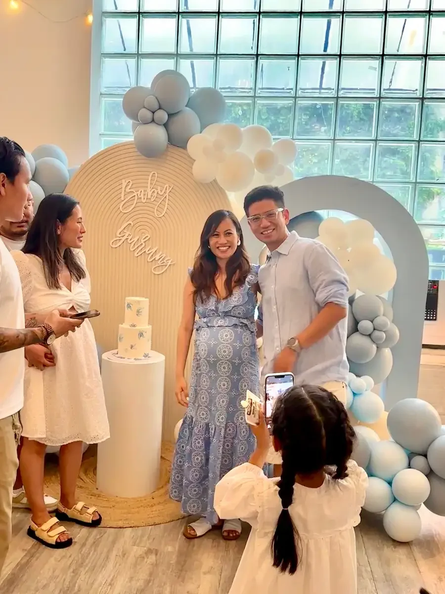 Baby shower setup at Bat Haus Brooklyn with balloon arch backdrop placed in front of the glass window wall, styled cake pedestal, and guests posing for photos.