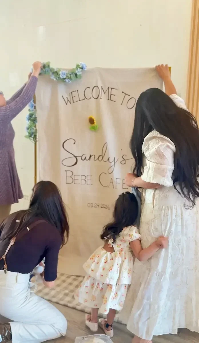 Hosts hanging a custom 'Welcome' baby shower backdrop banner at Bat Haus in Williamsburg, Brooklyn.