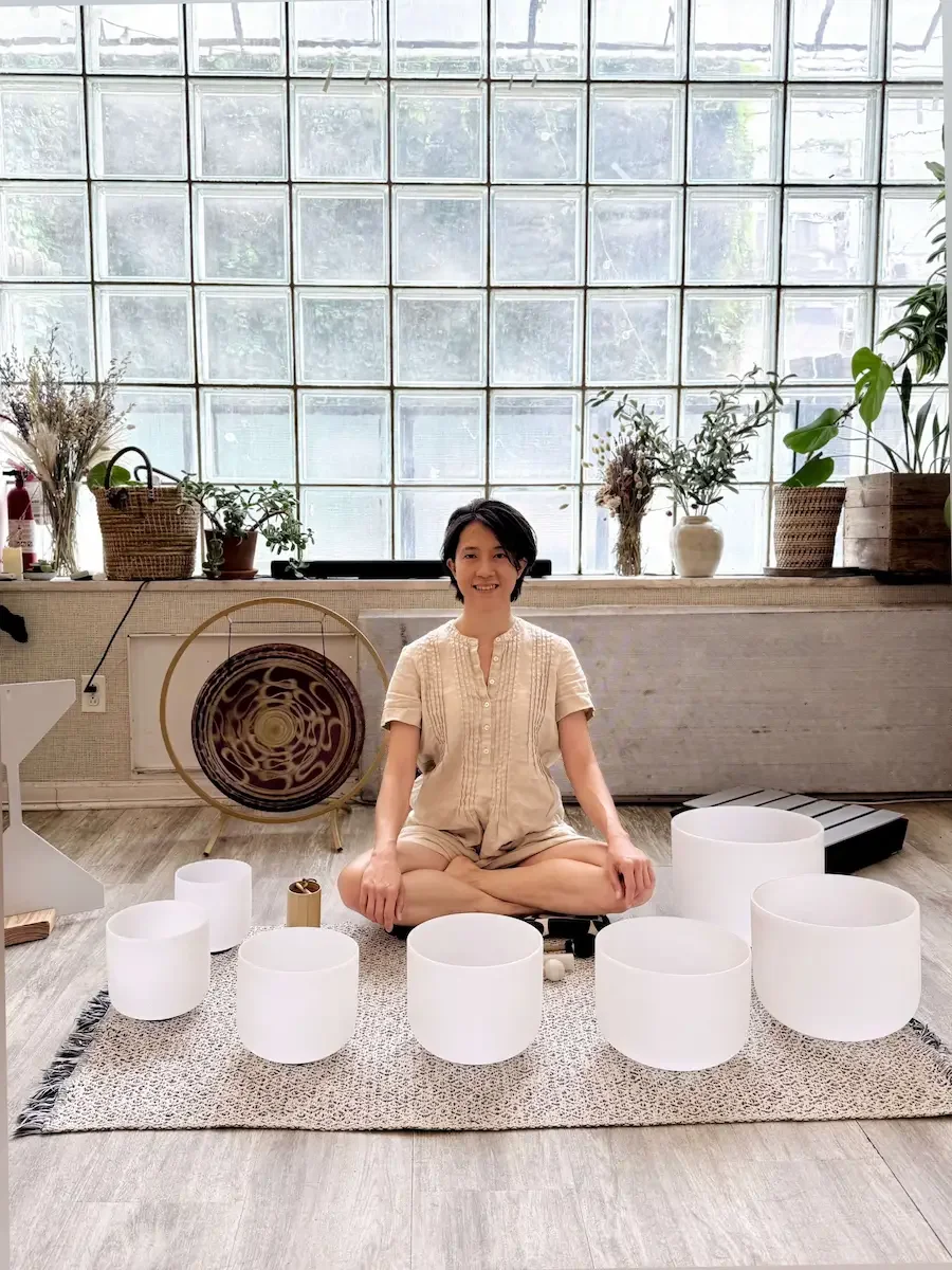 Practitioner seated among crystal singing bowls and a gong, ready to lead a corporate team sound bath wellness activity at Bat Haus in Brooklyn