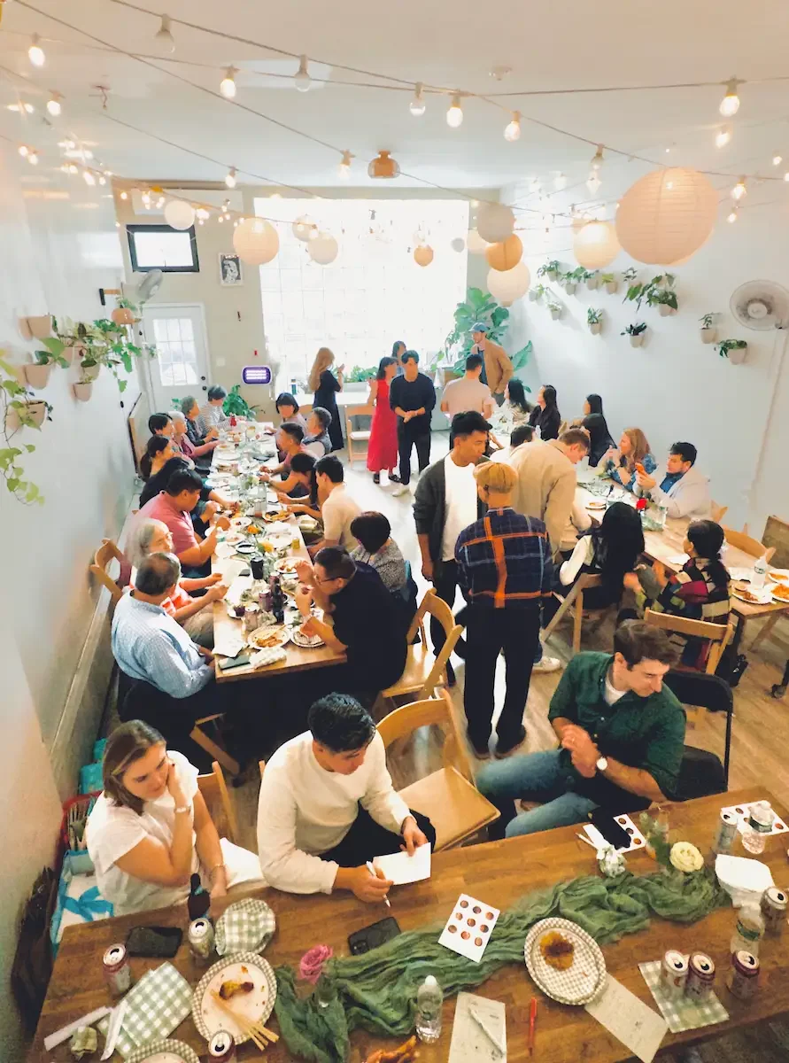 50-guest baby shower at Bat Haus in Williamsburg Brooklyn with long wooden tables, string lights, hanging lanterns, and indoor greenery during a seated celebration