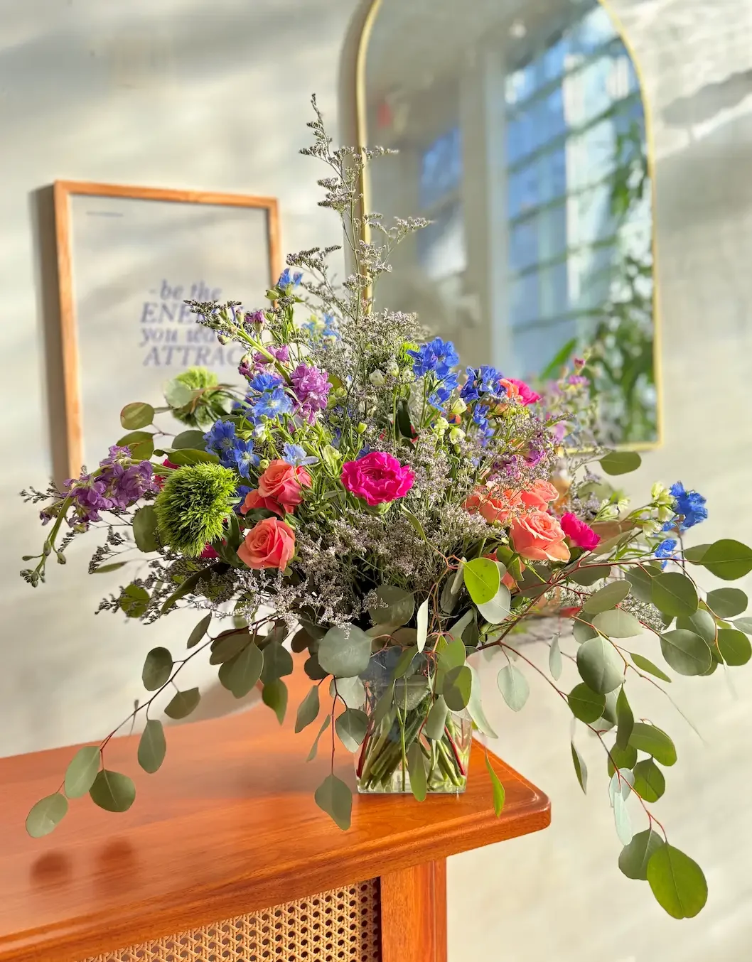 Wildflower-style arrangement with blue delphinium, pink roses, and trailing eucalyptus — in-house florals at Bat Haus in Williamsburg, Brooklyn.