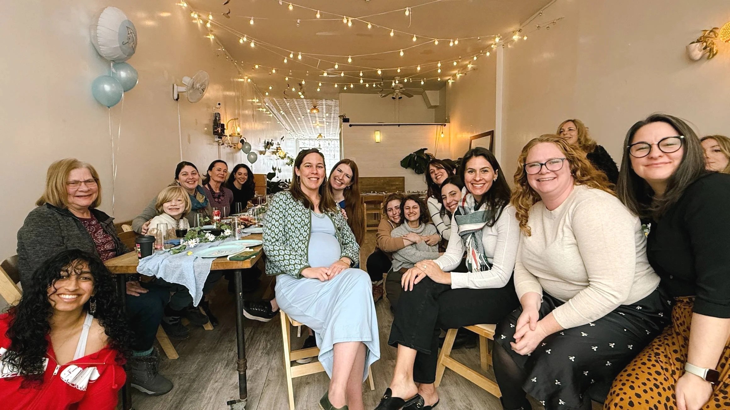 Baby shower celebration at Bat Haus Brooklyn event space with guests gathered around long wooden tables under string lights in Williamsburg NYC