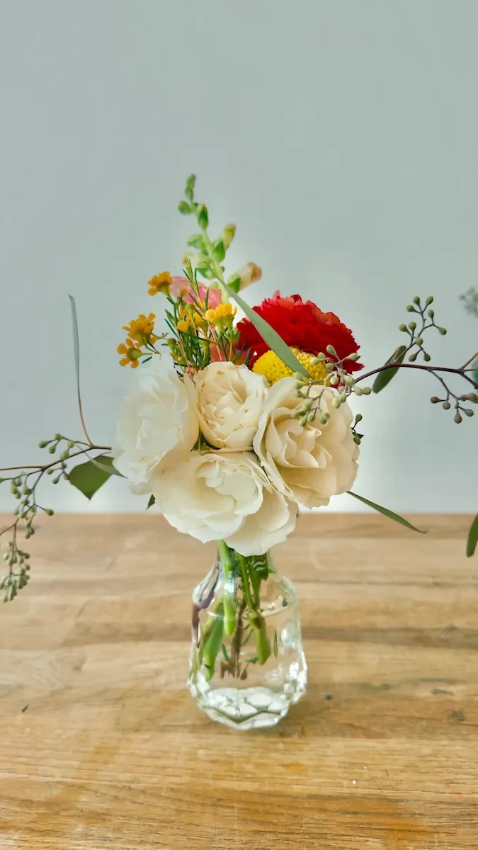 Cream garden rose and wildflower bud vase table floral in a glass vase at Bat Haus event space in Williamsburg, Brooklyn.
