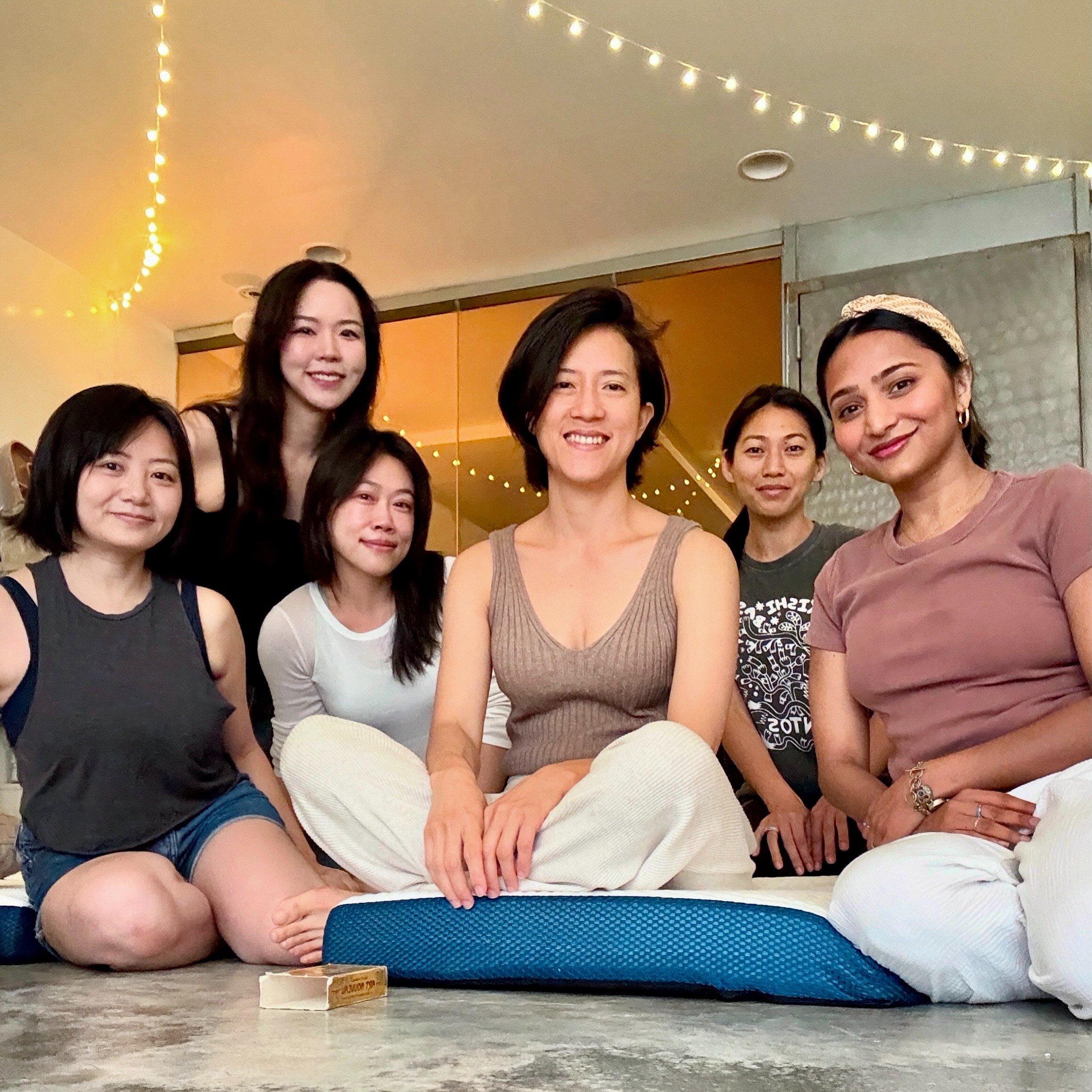 A smiling group seated on cushions in the warm, softly lit studio after a sound bath at Bat Haus in Williamsburg, Brooklyn.