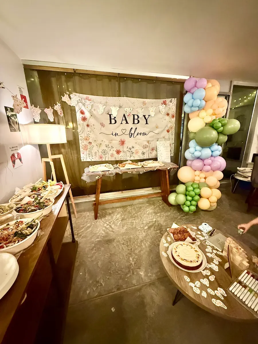 Downstairs studio set for a baby shower with a 'Baby in Bloom' backdrop, balloon arch, and food display at Bat Haus in Brooklyn.