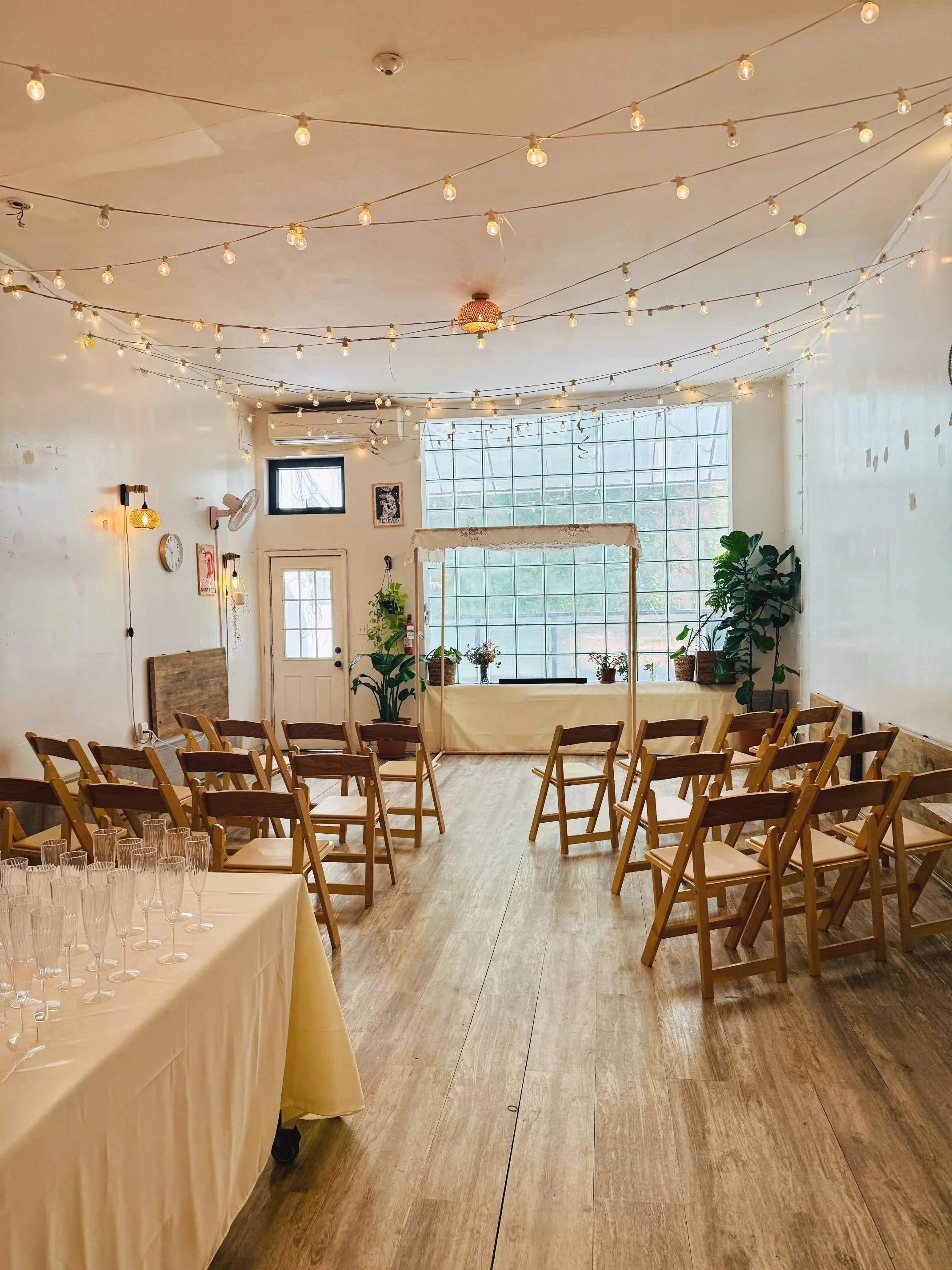 Chuppah setup for a Jewish wedding ceremony at Bat Haus in Brooklyn, featuring wooden chairs, warm string lights, natural light, and an intimate, minimalist event space.