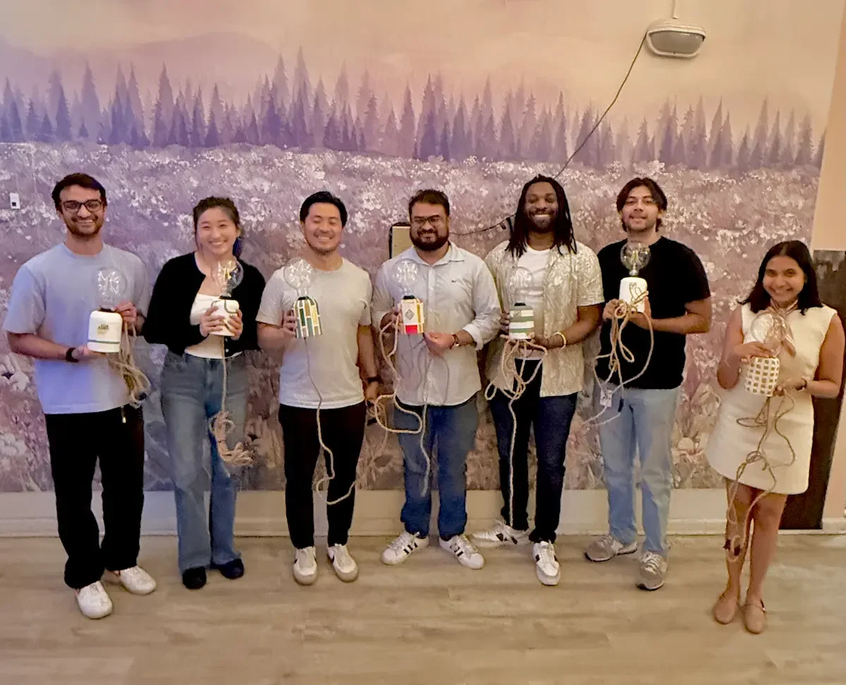 Uber team of seven smiling colleagues holding their handmade lamps after a lamp-making workshop at Bat Haus in Brooklyn