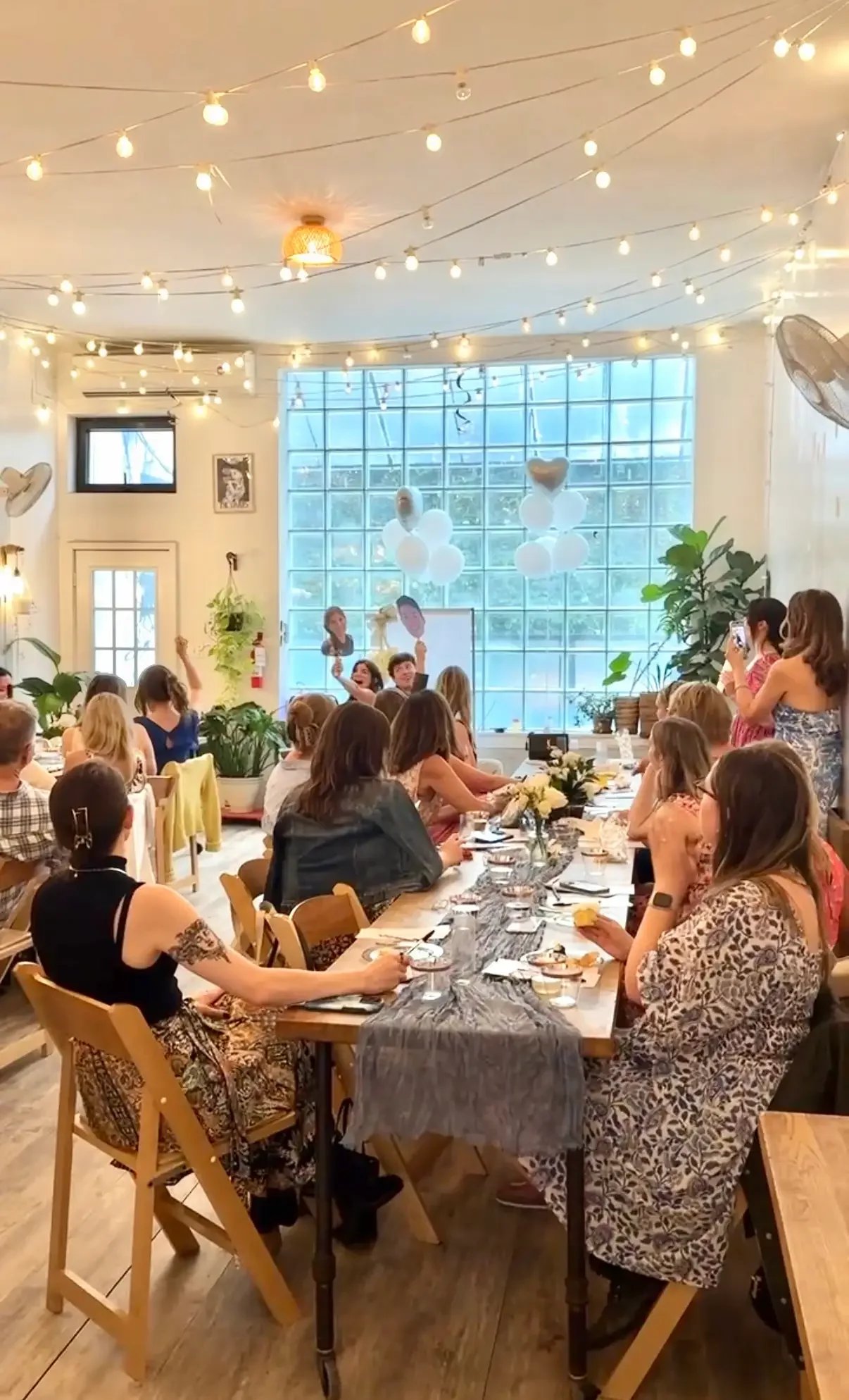 Bridal shower guests seated at a long table under string lights at Bat Haus, a Brooklyn bridal shower venue in Williamsburg.