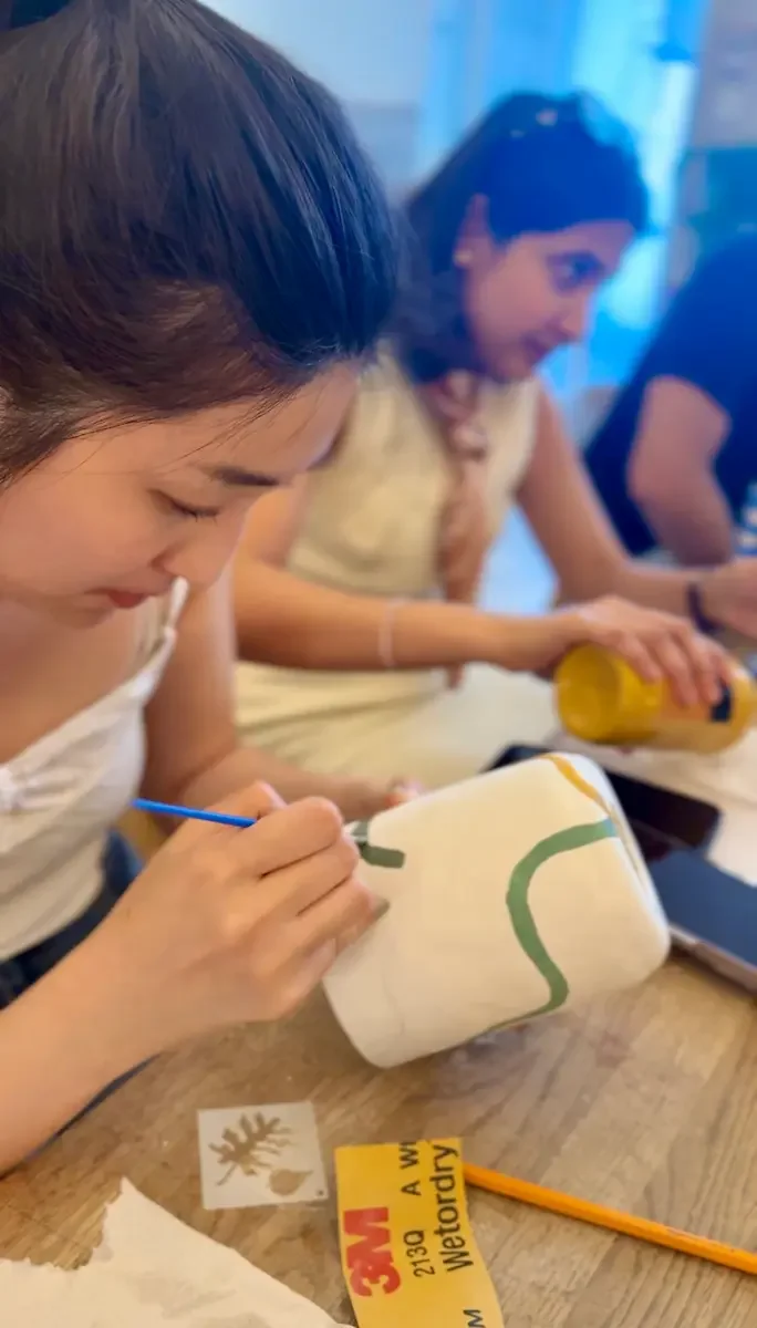 A guest carefully painting a green design onto a white lamp with a fine brush.