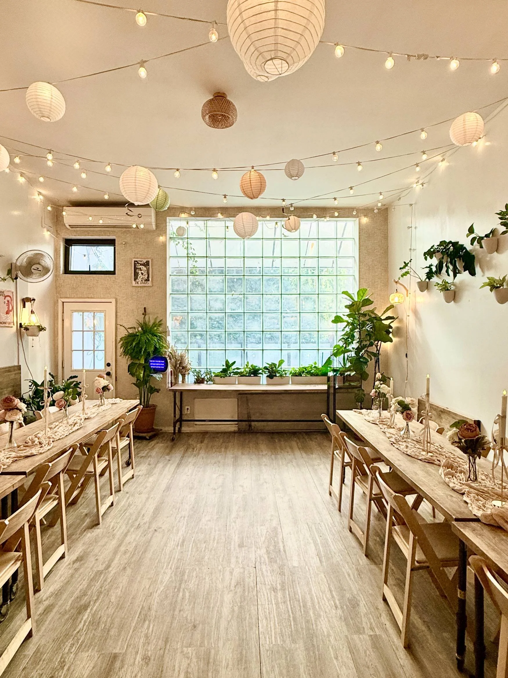 Warm wood tables and chairs with plants and string lights in a light-filled Brooklyn event space—Simple Package at Bat Haus.