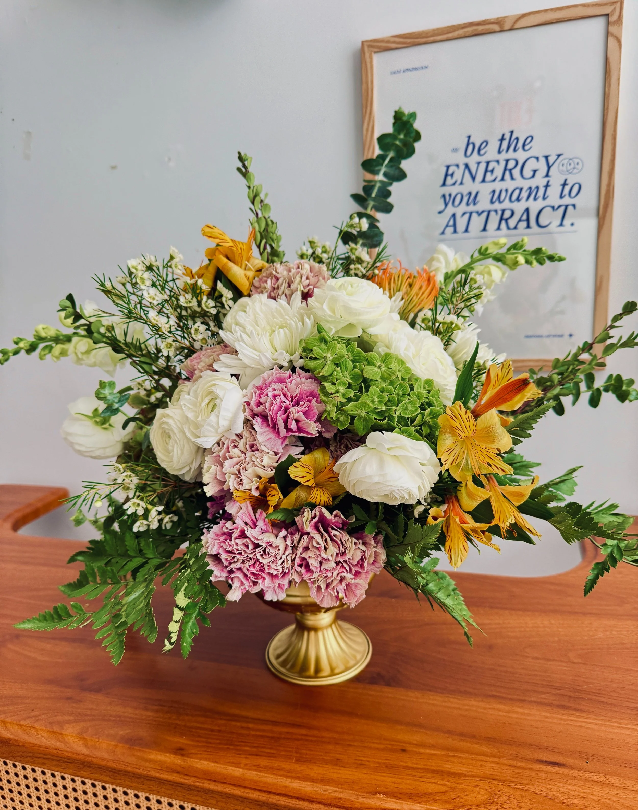 Signature Entryway Florals — Garden Classic (Cream + Blush + Citrus)
A lush, garden-style entry arrangement in a gold compote. Cream ranunculus and mums mingle with blush ruffles, green hydrangea, and citrus pops of alstroemeria, finished with fern
