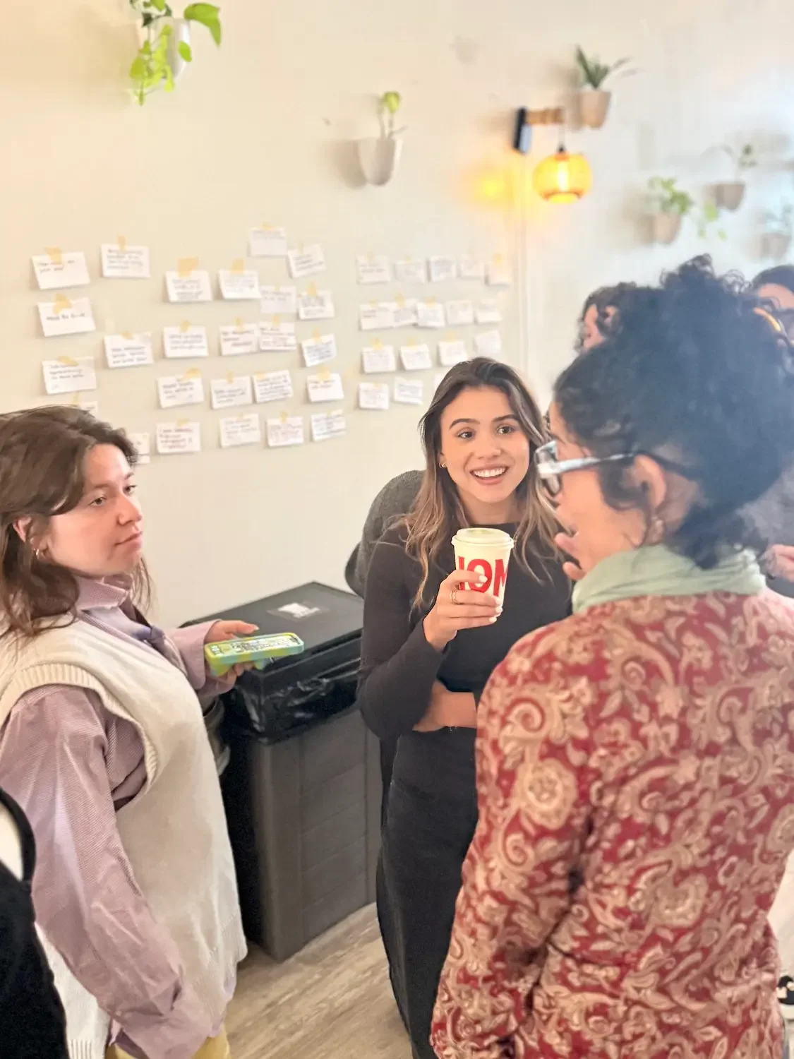 Colleagues talking over coffee beside a sticky-note brainstorm wall during a corporate offsite at Bat Haus in Williamsburg, Brooklyn.