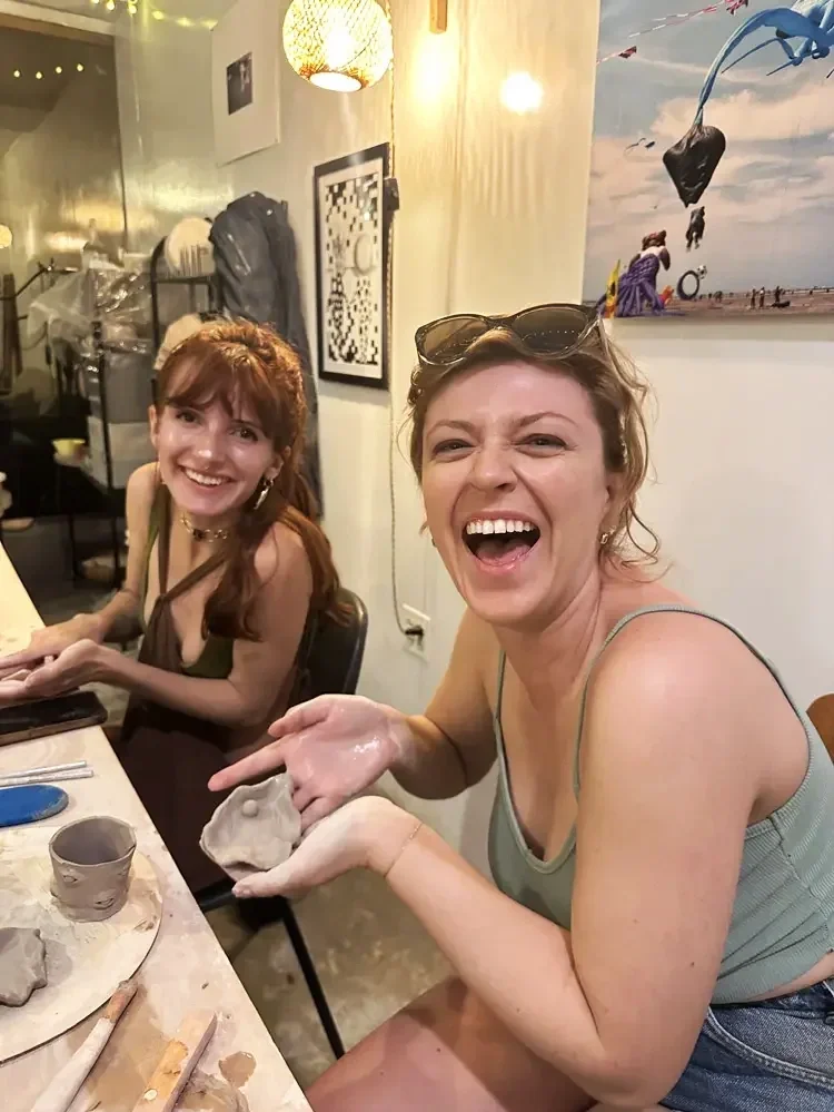 A laughing guest hand-building a small clay jewelry dish at a pottery class at Bat Haus in Williamsburg, Brooklyn.