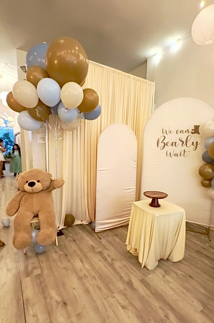 Styled baby shower setup at Bat Haus with a cream balloon arch, 'We Can Bearly Wait' backdrop, and dessert table in the Williamsburg event space