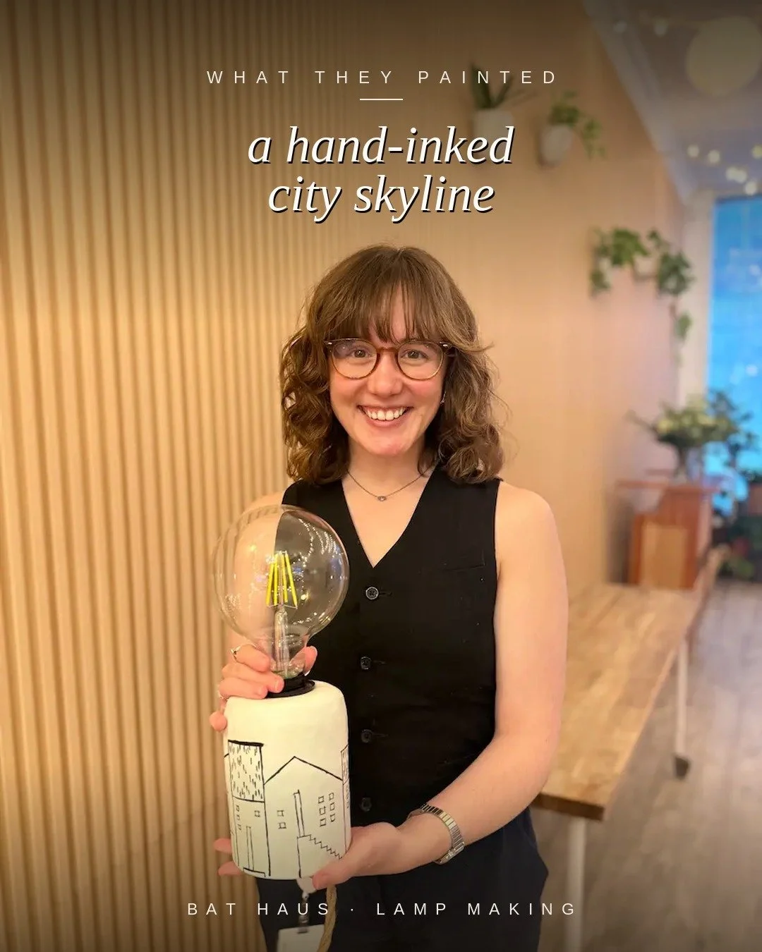 Guest holding a lamp decorated with a hand-inked city skyline of small houses and buildings.