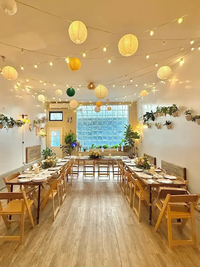 Bat Haus Brooklyn event space interior with long wooden tables, string lights, and glass block windows, showcasing flexible event packages for weddings, private parties, and corporate offsites.