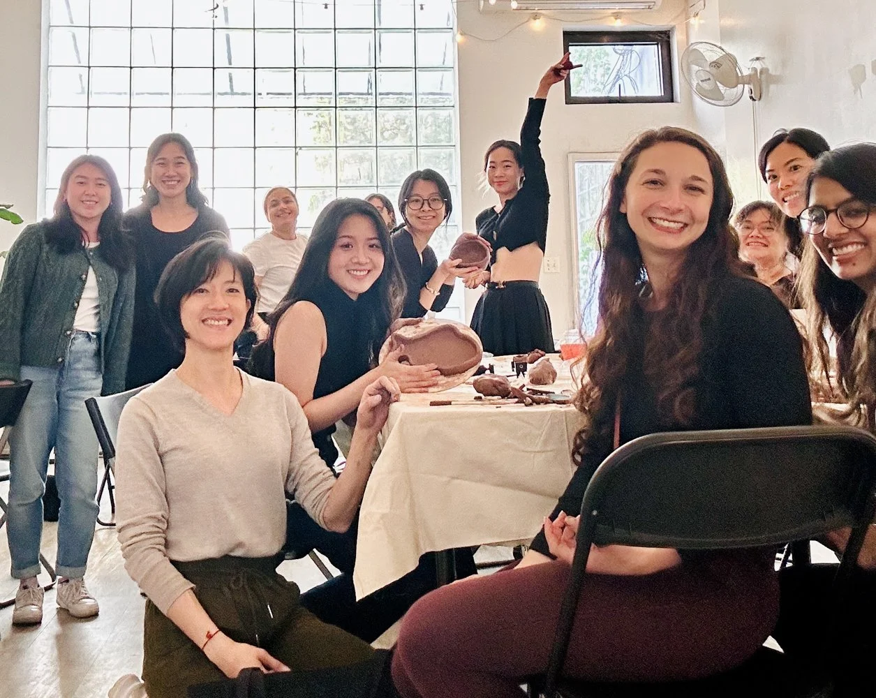 Group of participants smiling and holding handmade clay bowls during an enhanced experience hand building pottery class at Bat Haus in Williamsburg Brooklyn.