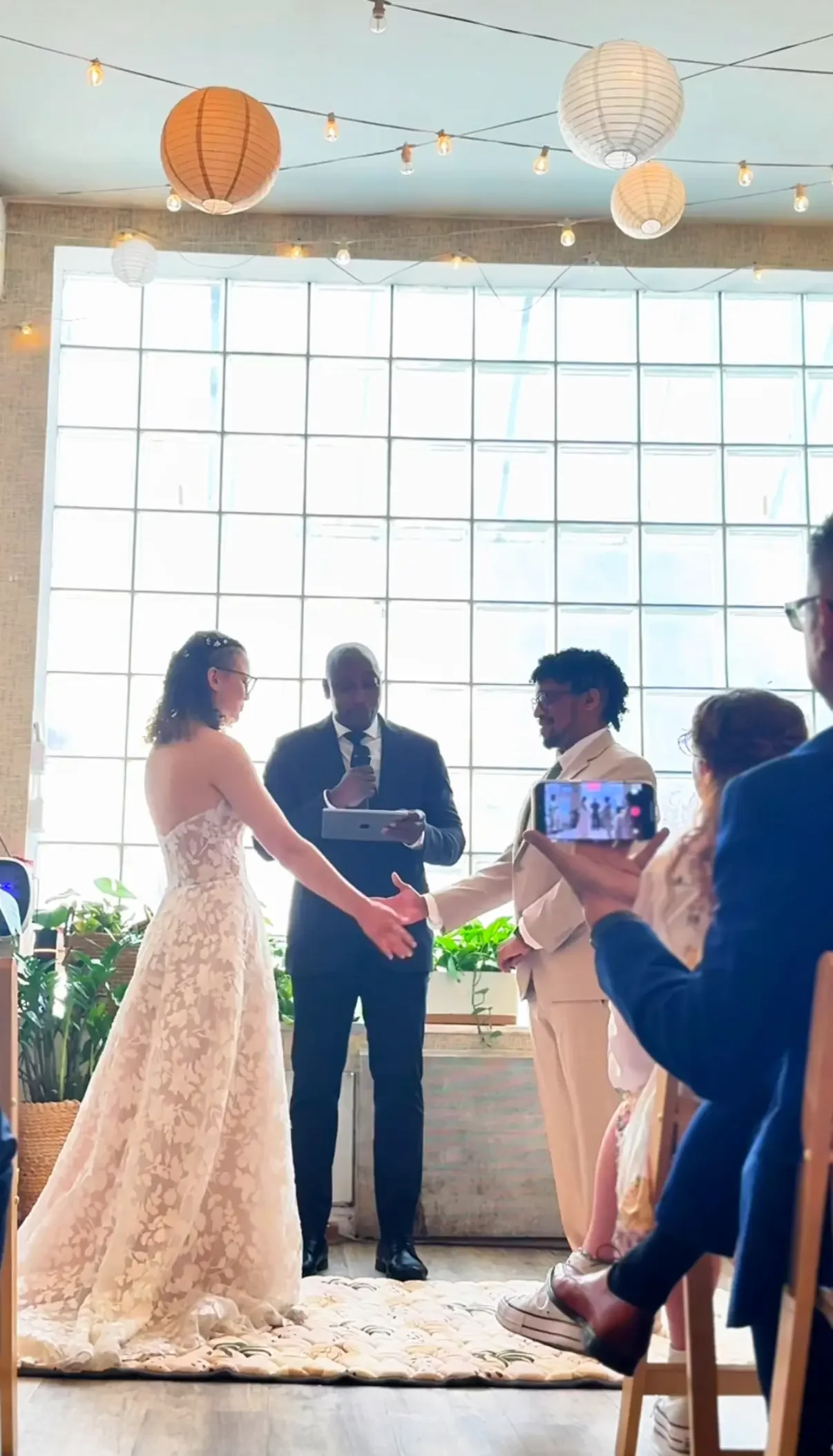 A couple holding hands during their wedding ceremony by the glass-block window at Bat Haus in Williamsburg, Brooklyn.