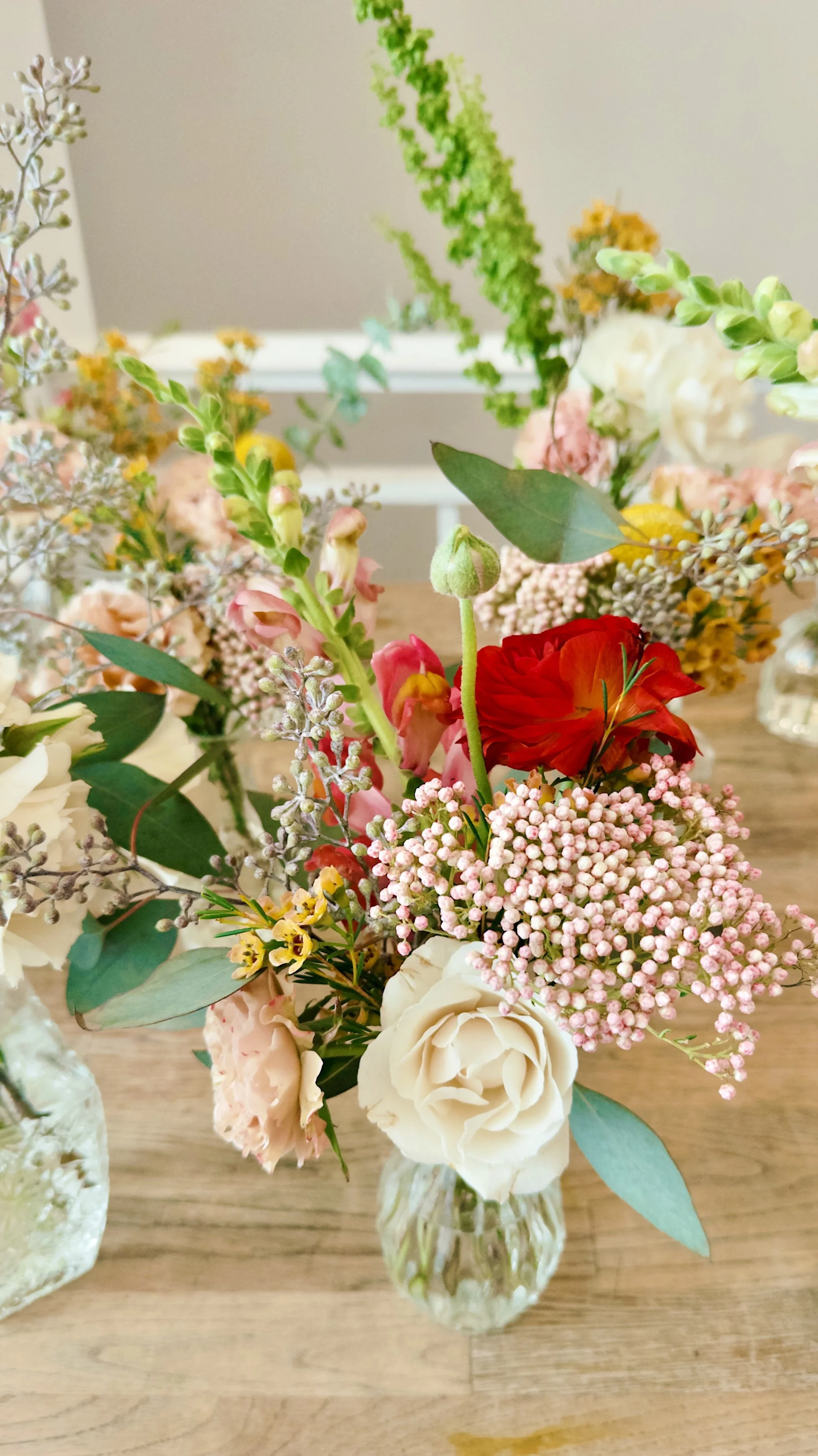 Seasonal bud vase floral arrangements included in the Styled package at Bat Haus in Brooklyn displayed on wooden banquet tables.