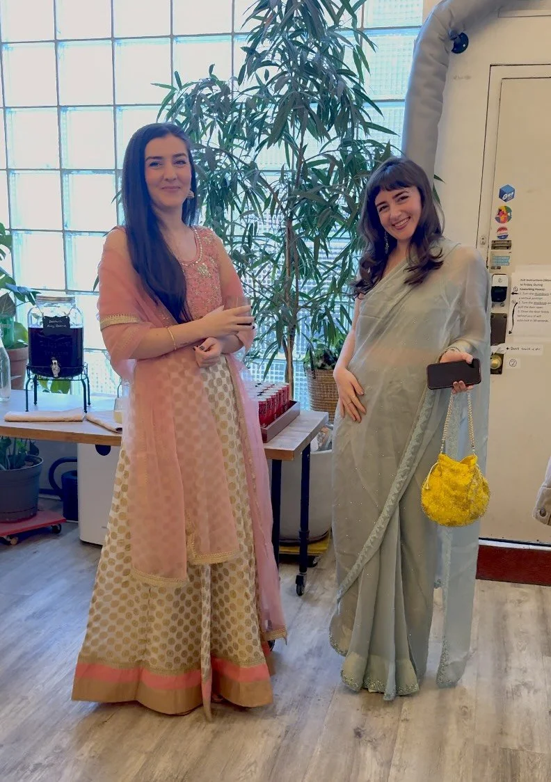 Two wedding guests in a pink and gold anarkali with dupatta and a pale blue saree standing by the drink station and glass-block window at a Nikah celebration at Bat Haus in Williamsburg, Brooklyn