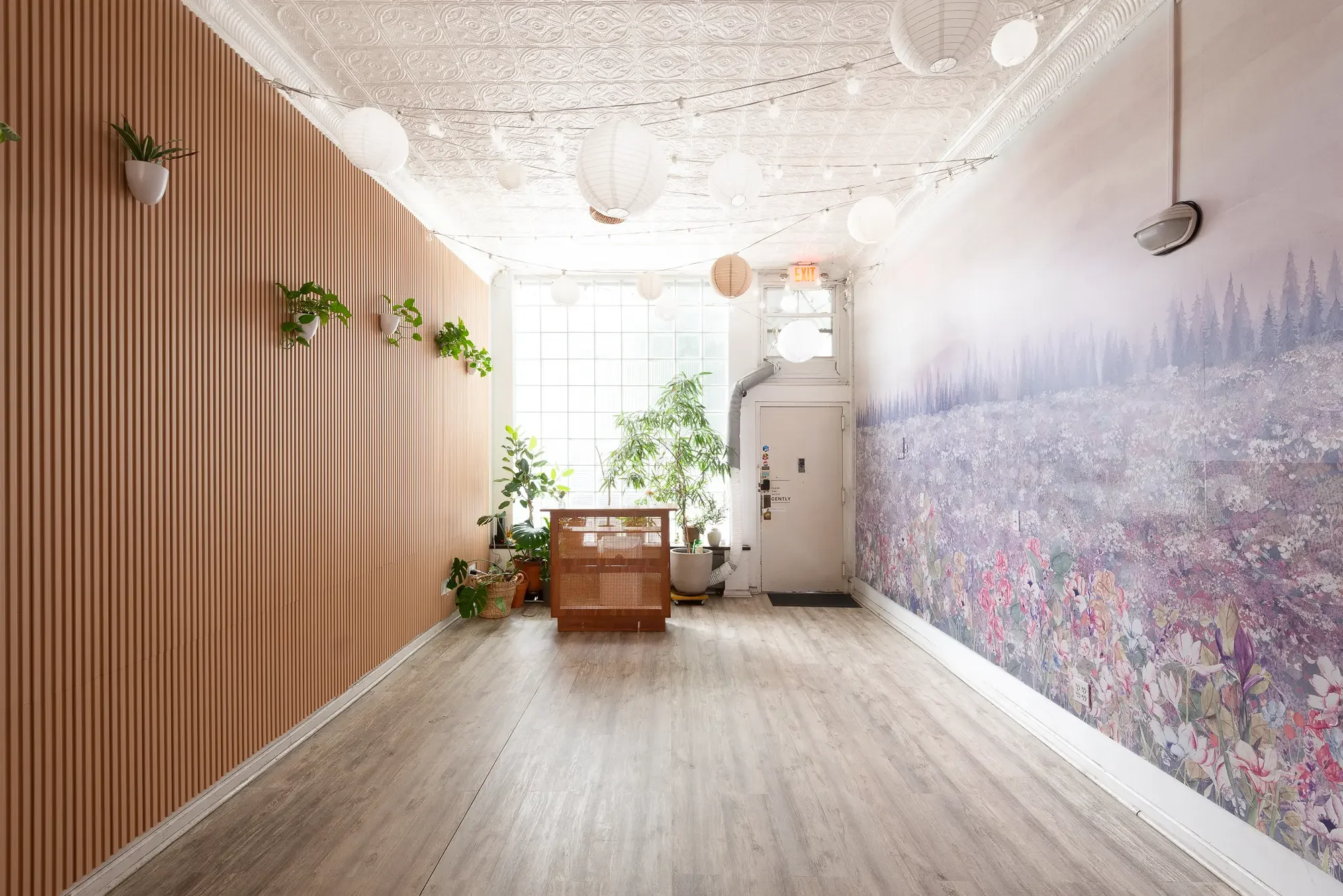 Entrance of Bat Haus holiday party venue in Williamsburg, Brooklyn, with paper lanterns, a floral mural, and natural light from the glass-block window