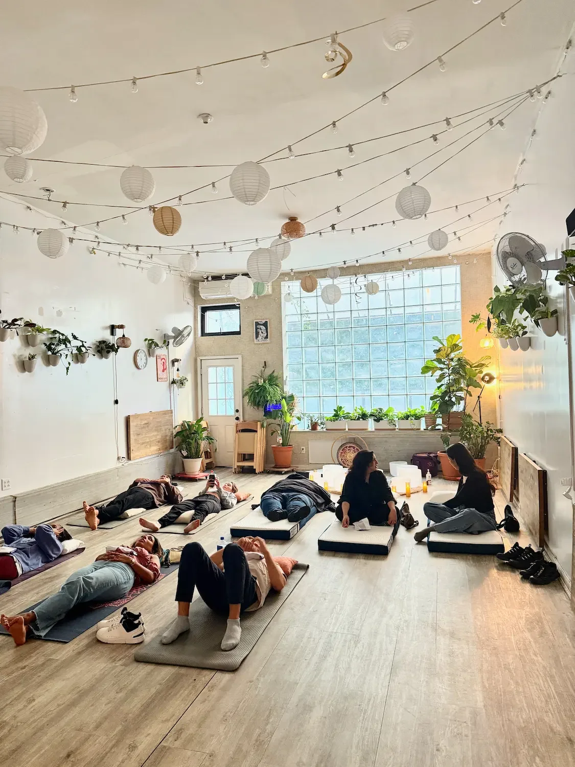 Participants resting on mats during a weekday wellness event in the calm, string-lit Bat Haus studio in Williamsburg, Brooklyn.