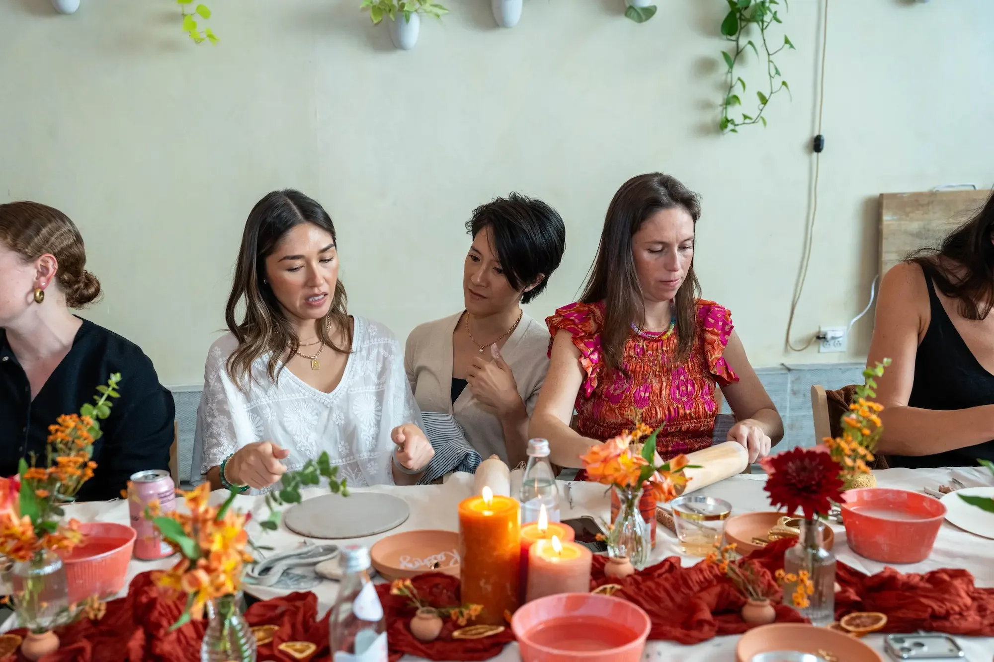 Guests rolling out slabs of clay at a pottery class in Williamsburg, Brooklyn, with orange roses, dahlias, and lit candles down the table.