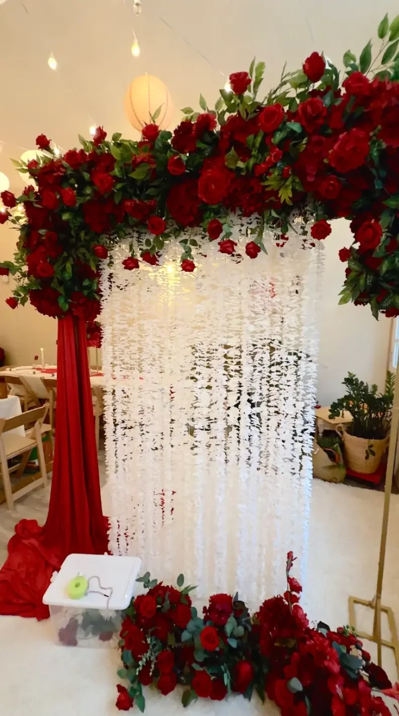 Ceremony backdrop of deep red roses and greenery with a white hanging blossom curtain and red draped fabric, set up for a Nikah celebration at Bat Haus in Williamsburg, Brooklyn
