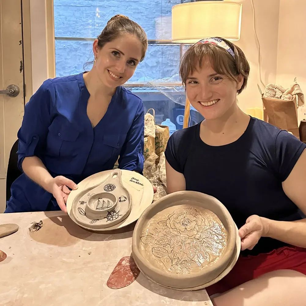 Two guests showing the decorative dinner plates they made at a hand-building pottery class at Bat Haus in Williamsburg, Brooklyn.