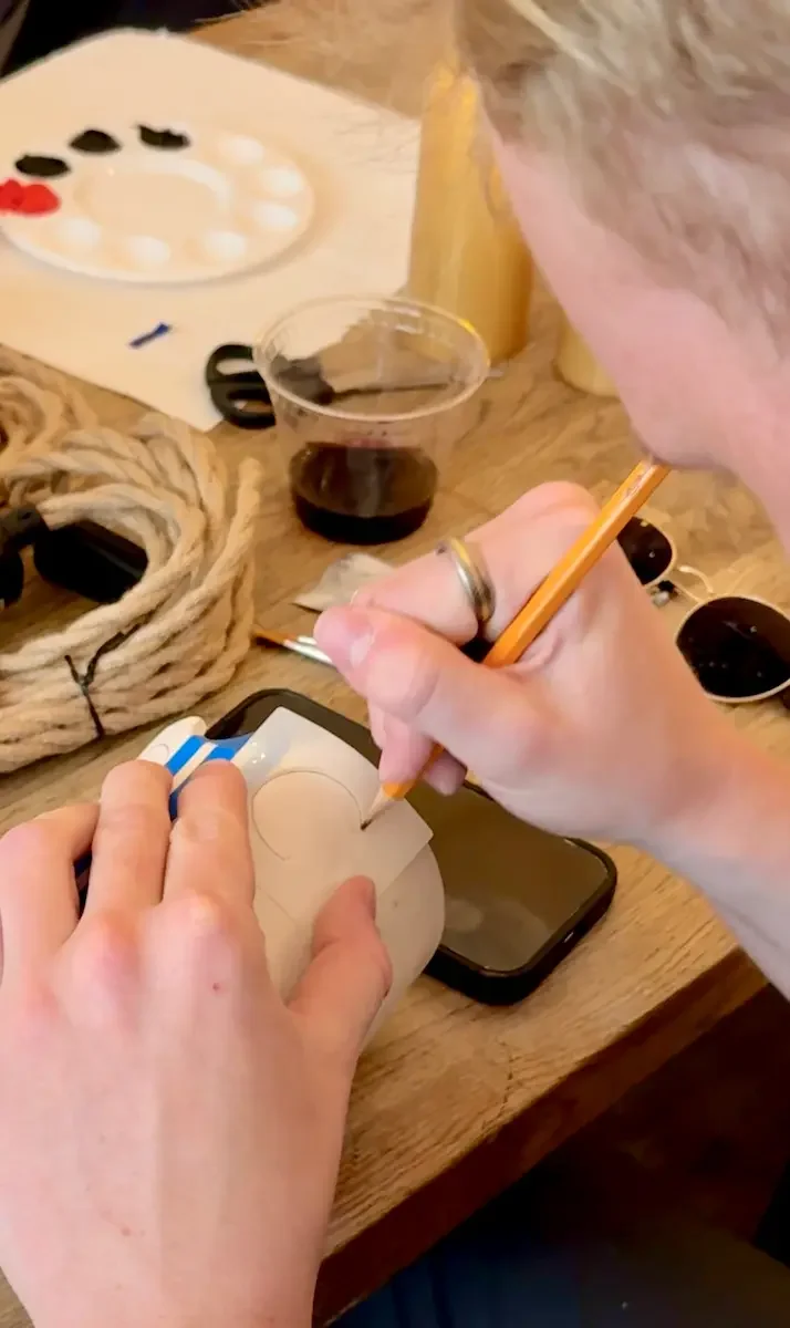Hands using a pencil to trace a stencil shape onto a small lamp base.