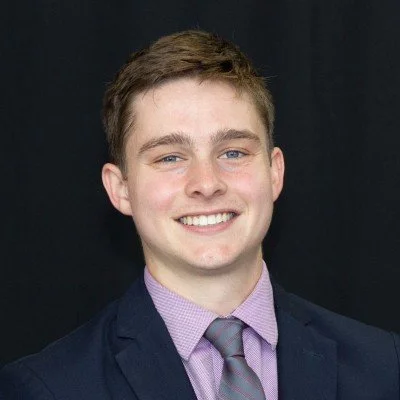 Man in a suit smiling against a black background.