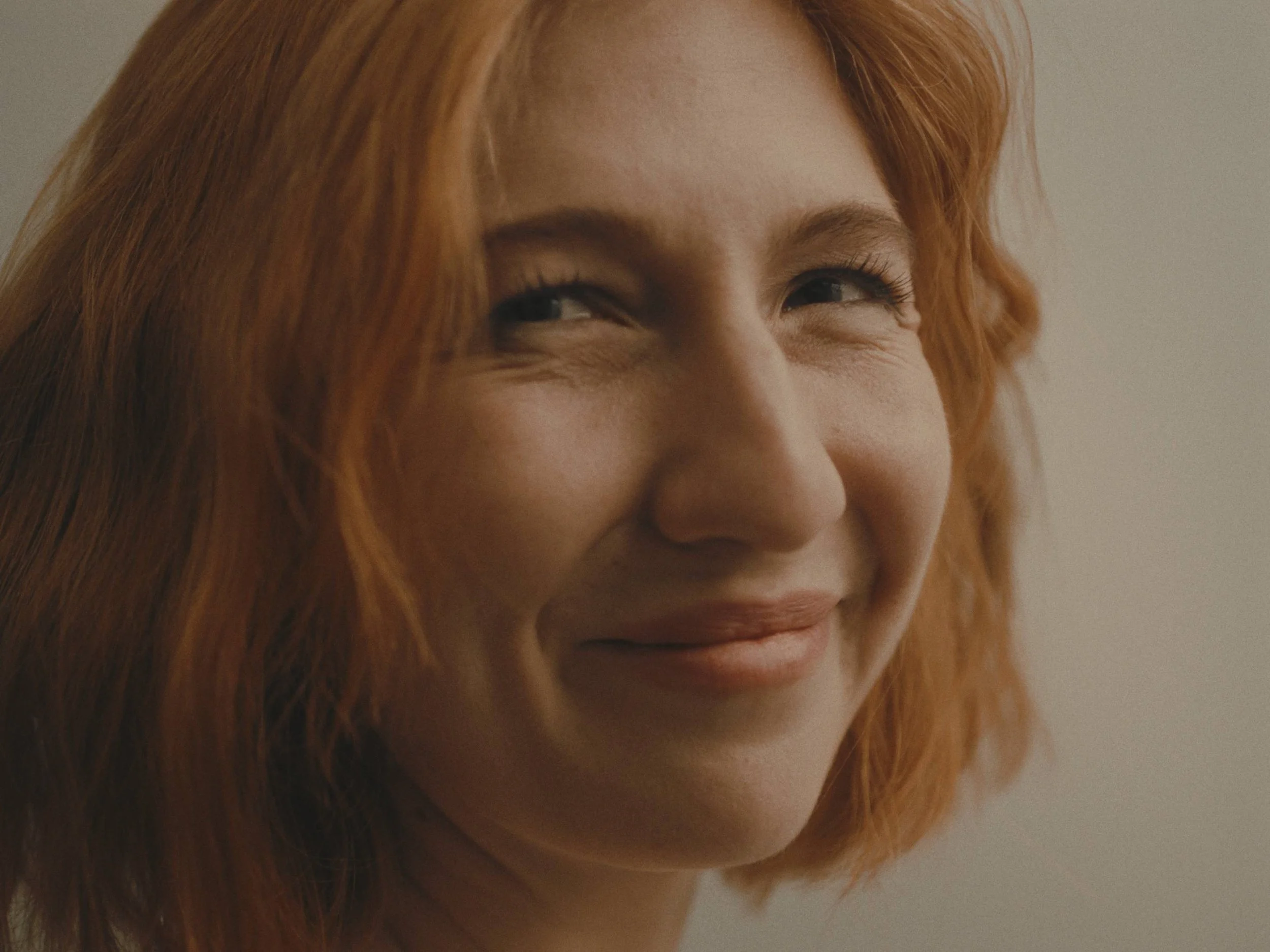 Close-up of a woman with red hair smiling softly, looking slightly to the side.