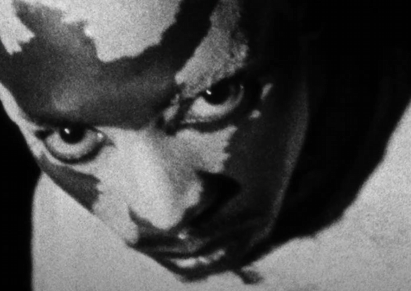 Close-up black and white photograph of a person with intense eyes, partially covering their face with a hand.