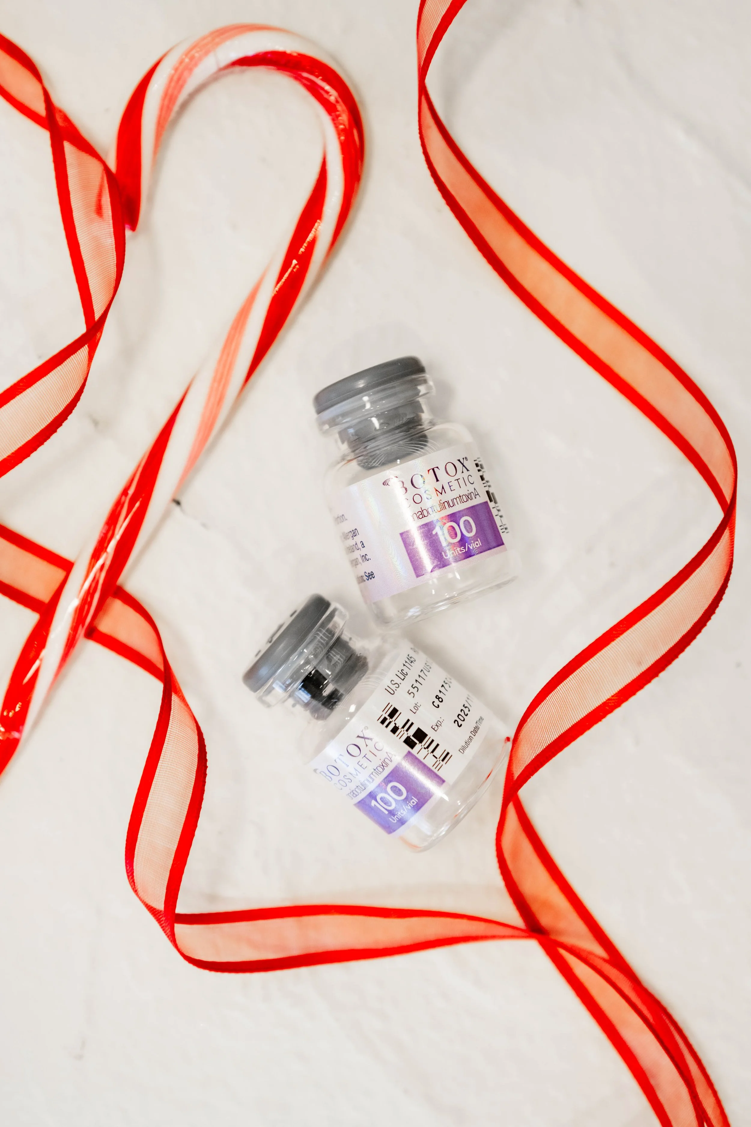Two small bottles of Botox cosmetic with purple labels, surrounded by red and cream striped ribbons on a white background.