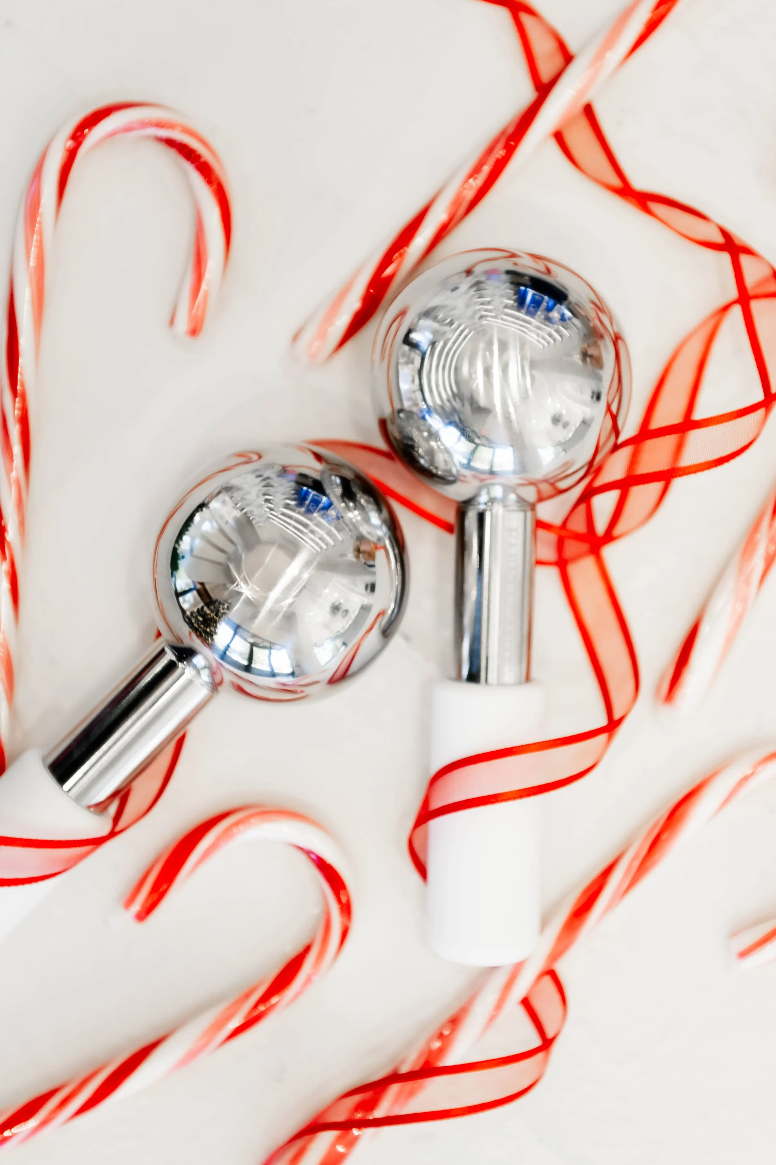 Two chrome Christmas ornaments, candy canes, and a white and silver Christmas cracker arranged on a white surface.