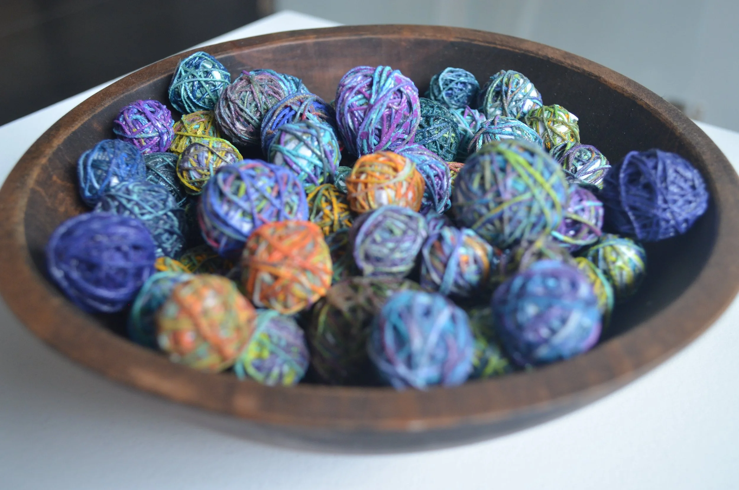 Wooden bowl filled with colorful yarn balls in shades of blue, purple, orange, and green.