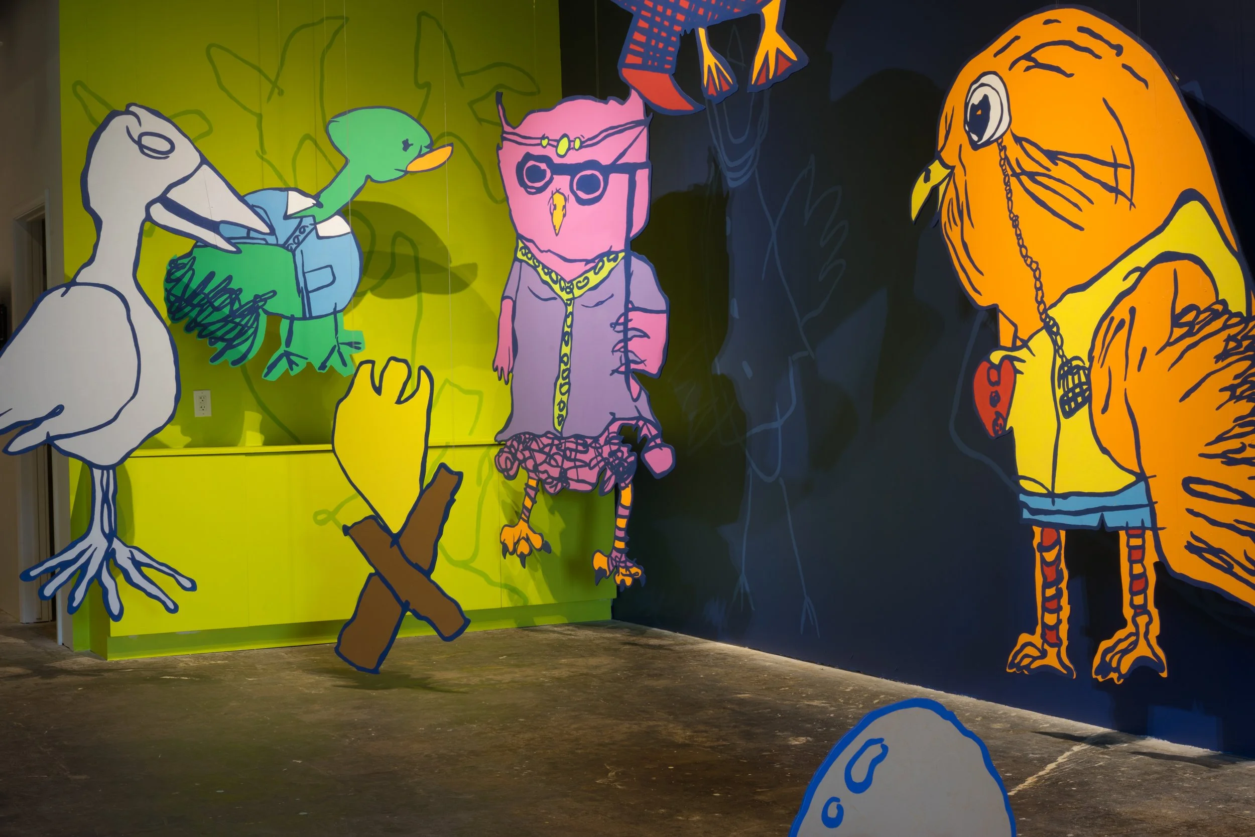 Colorful mural of stylized cartoon characters on a wall, including a heron, a duck, an owl, and a large orange bird with a chain necklace. The background has bright green and dark blue sections with abstract designs.