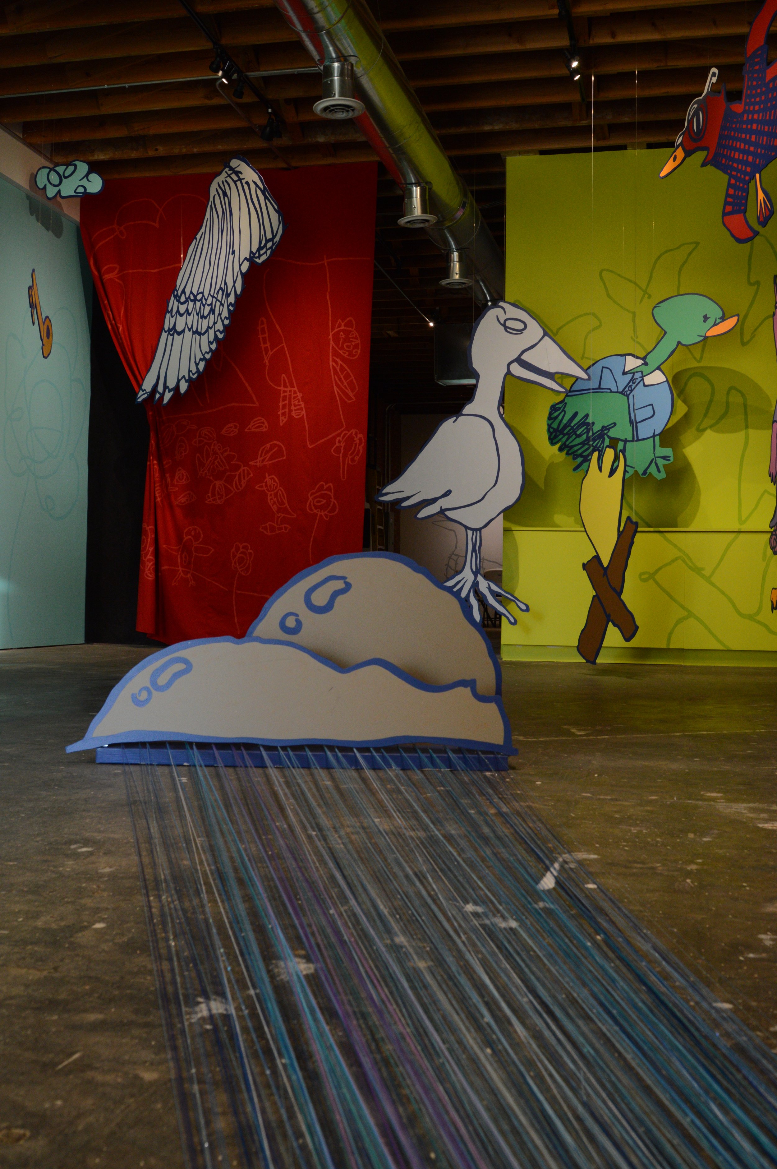 Art installation featuring cartoon-like seagulls, wings, and a duck on a colorful backdrop with artistic sketches and drawings.