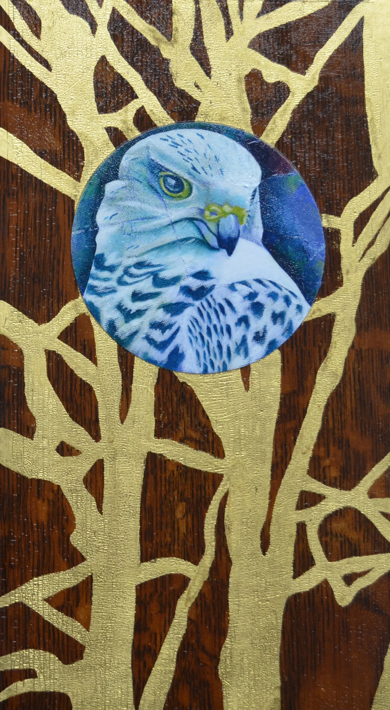 A circular sticker featuring a detailed painting of a falcon's head is placed on a wooden surface with a gold floral pattern.