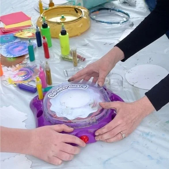 Two people playing with a Spin Master Shadow Guard drawing toy, surrounded by colorful markers, papers, and art supplies on a table.