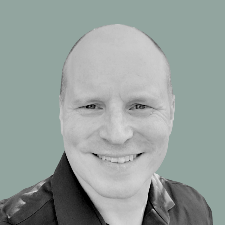 Black and white photo of smiling man with short hair, wearing a dark shirt, against a solid light background.