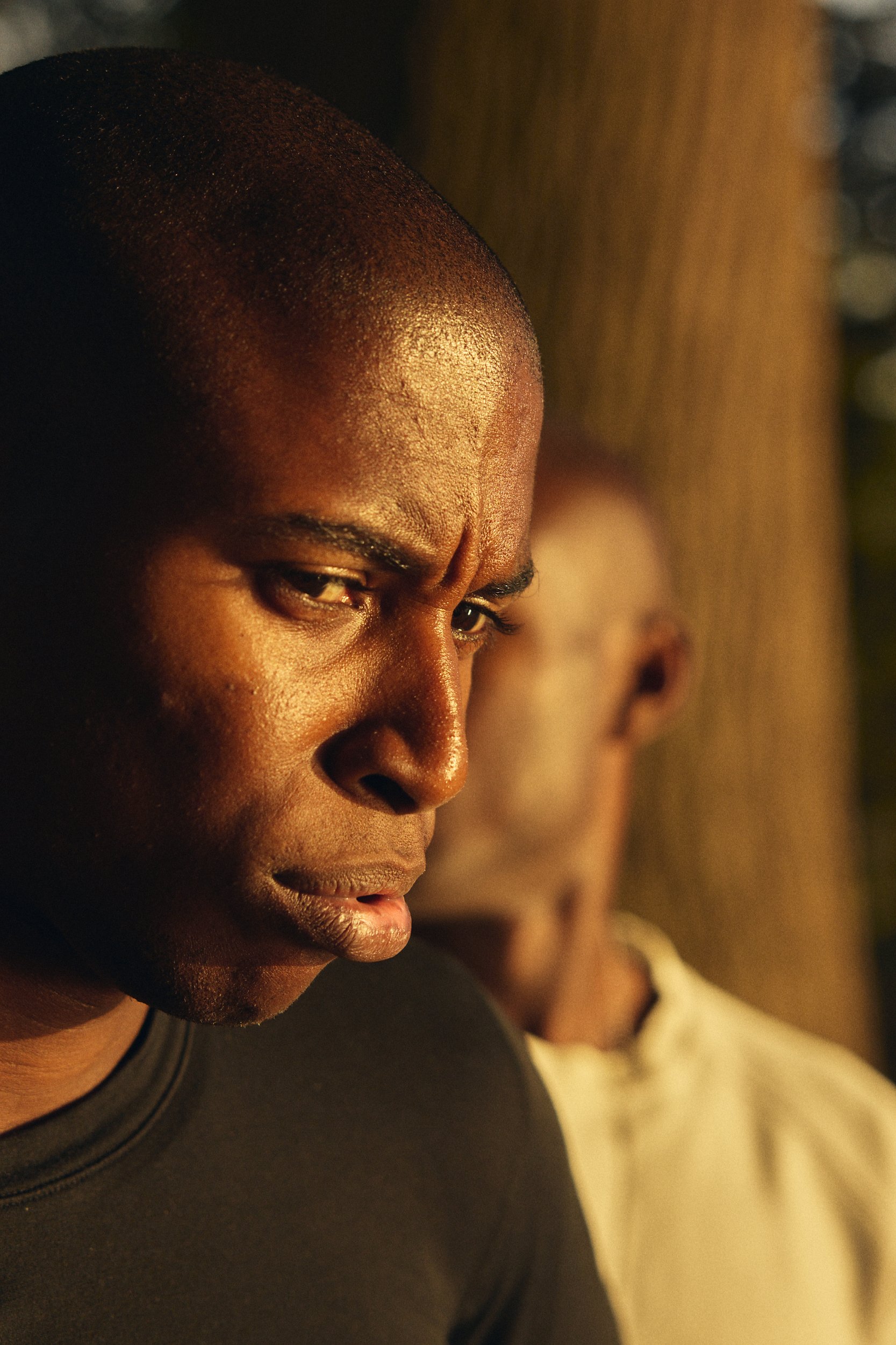 Close-up of a young man's face focusing on his forehead and eyes, with facial features and skin texture visible, and another person slightly blurred in the background.