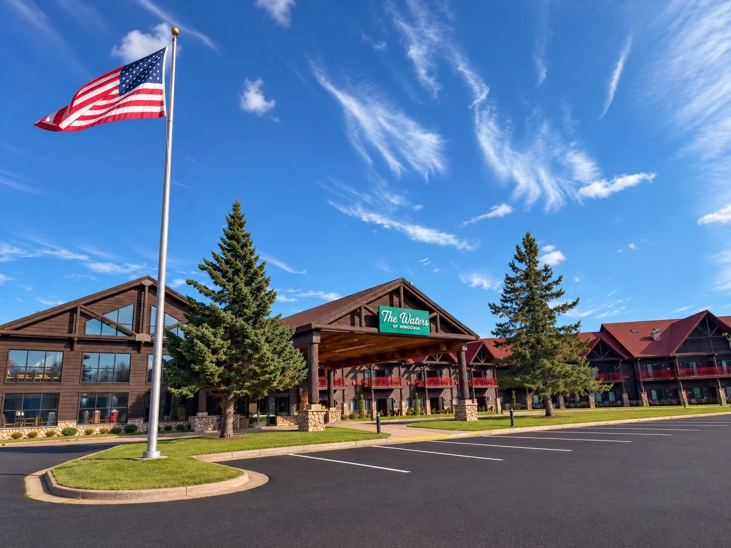 Exterior of The Waters of Minocqua lodge-style hotel with evergreen trees under a blue Northwoods sky